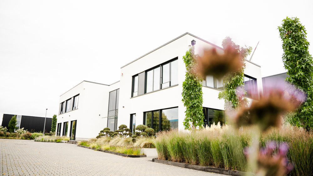Moderne Architektur mit wei&szlig;en W&auml;nden, gro&szlig;en Fenstern und gepflegtem Garten.